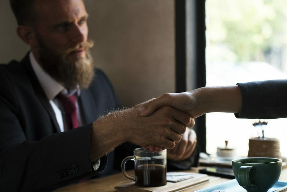 Man shaking another person's hand over coffee