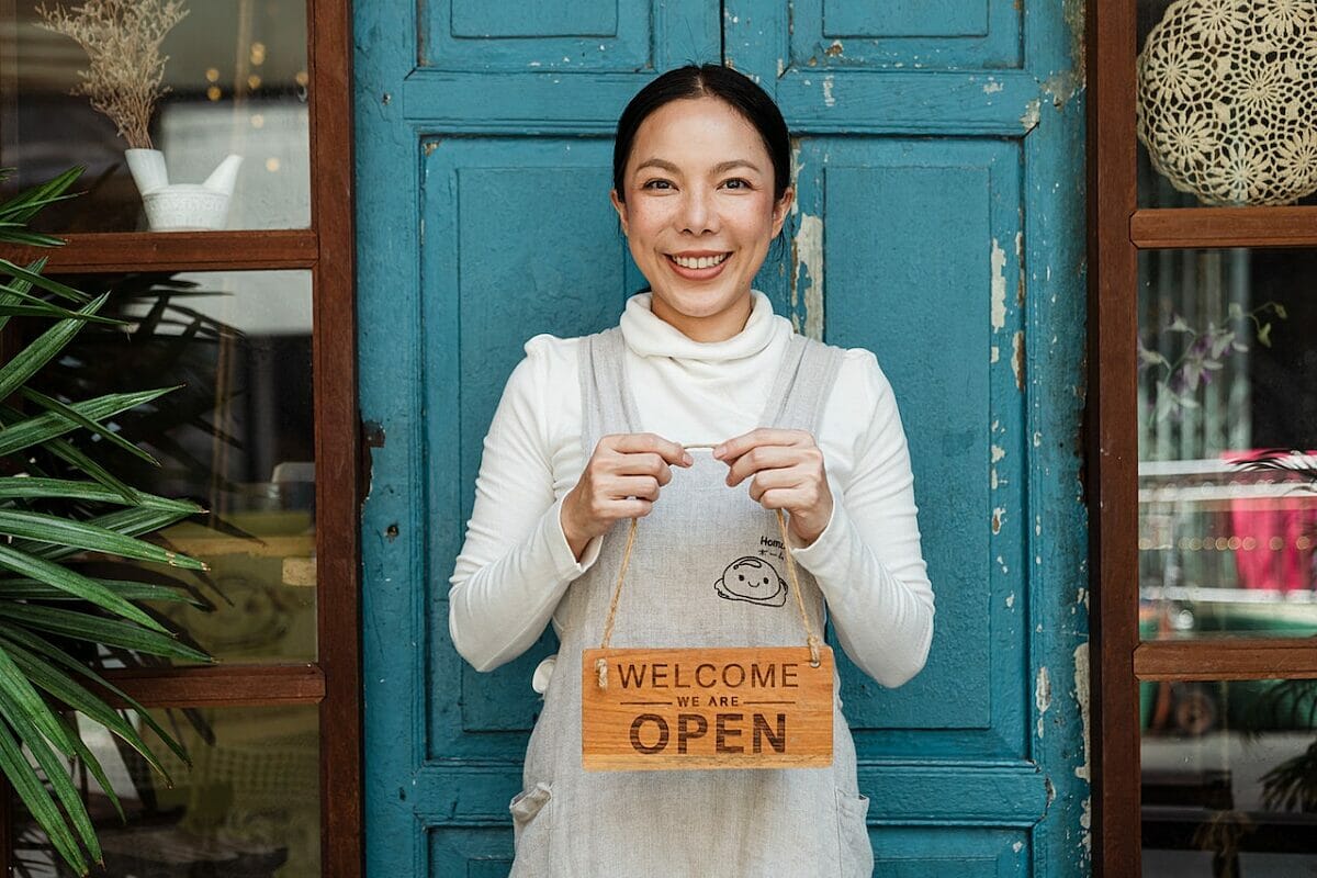 Woman smiling and holding a sign saying Welcome We Are Open